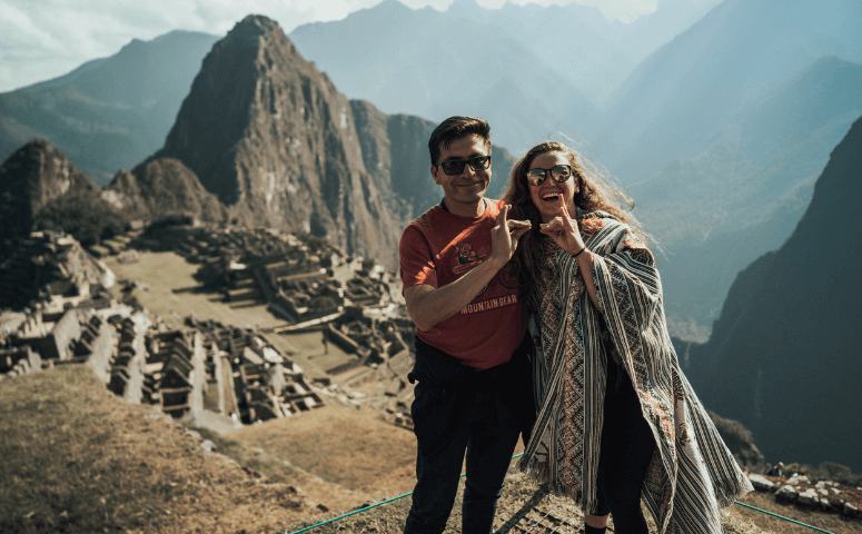 viajero con gafas de sol y poncho junto al guia frente a las ruinas de machu picchu